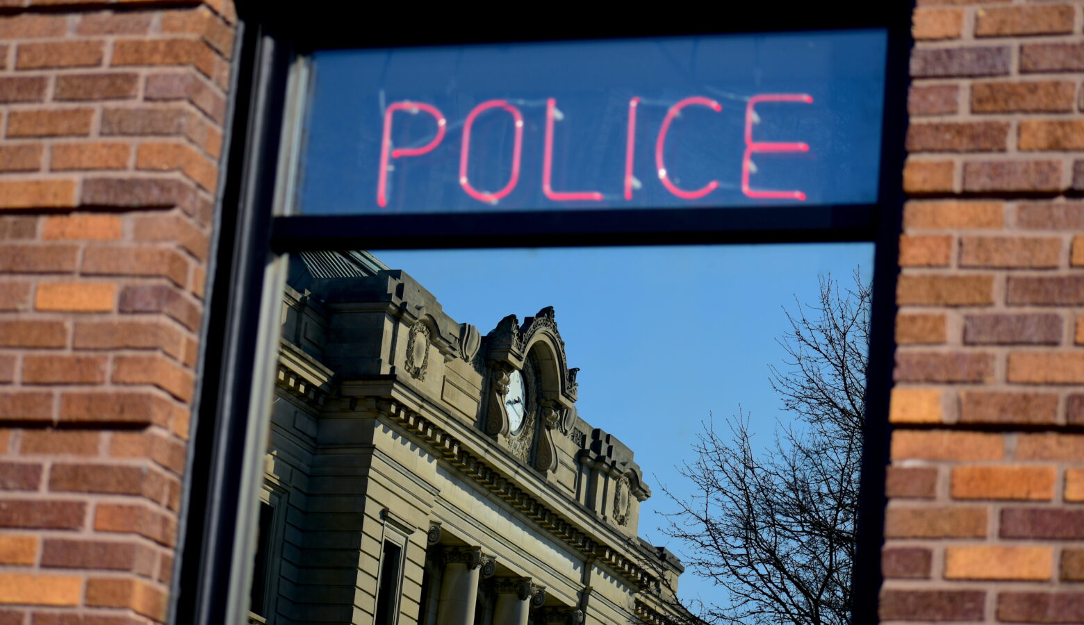 A neon sign in a window reads "Police." There is a county courthouse in the reflection of the window.