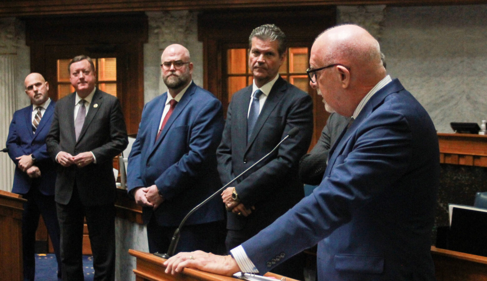 A line of lawmakers look on as one of their colleagues speaks at a lectern on the Indiana Senate floor.