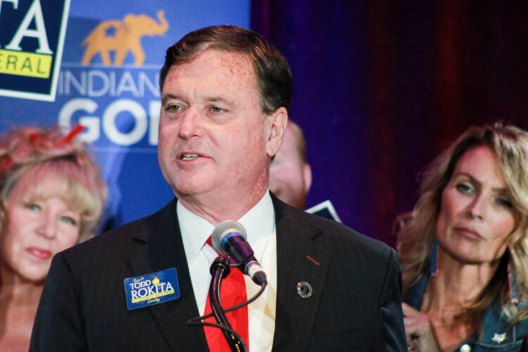 Todd Rokita speaks at a campaign event. Rokita is a White man with dark hair. He is wearing a black suit, white shirt and red tie.