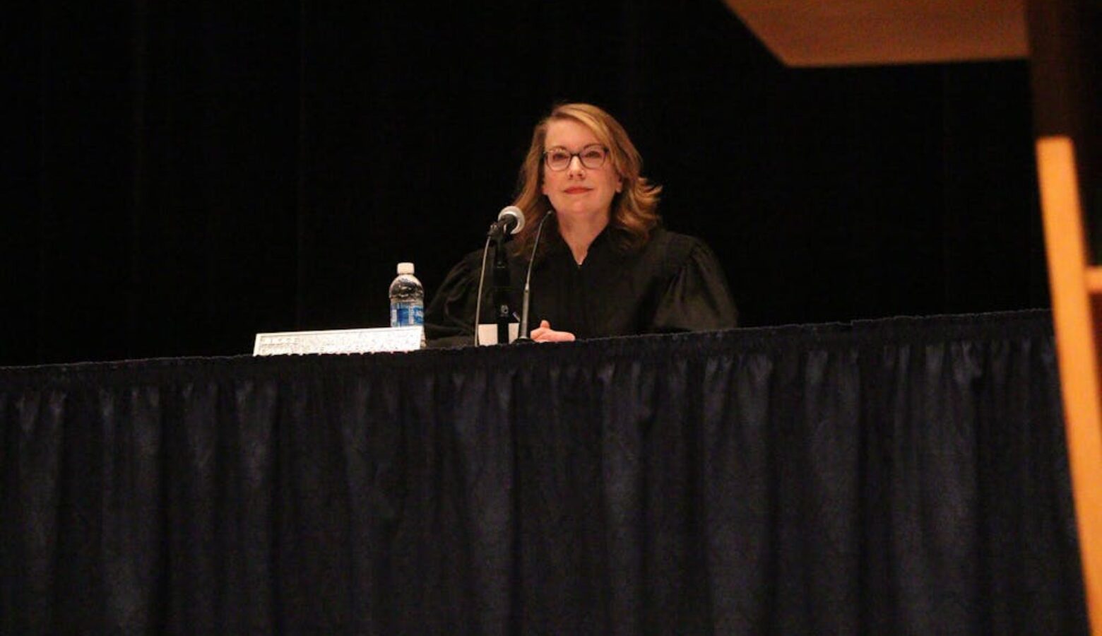 Judge Dana Kenworthy sits behind a table with a black tablecloth. She is a White woman with glasses, dressed in a black judge robe.