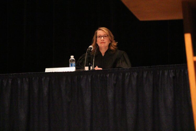 Judge Dana Kenworthy sits behind a table with a black tablecloth. She is a White woman with glasses, dressed in a black judge robe.