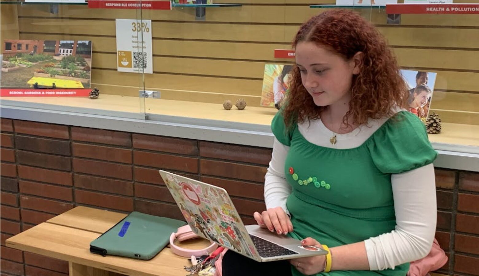 A White student with red curly hair sits on a bench, typing on a laptop in her lap.