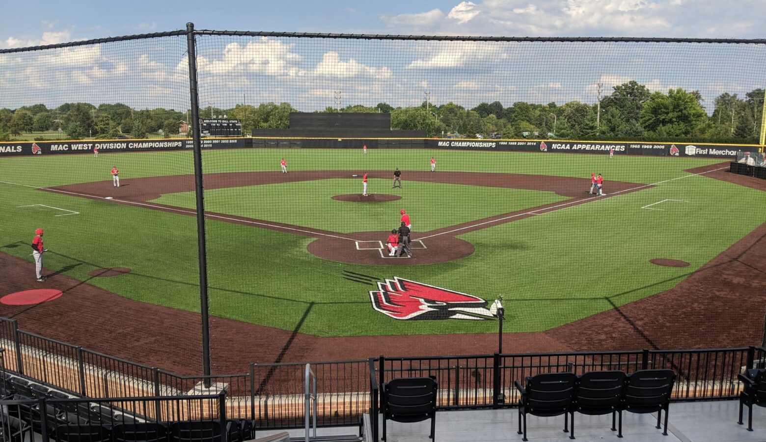 From the stands and behind a black fence, baseball players in red and white uniforms play on a baseball field.