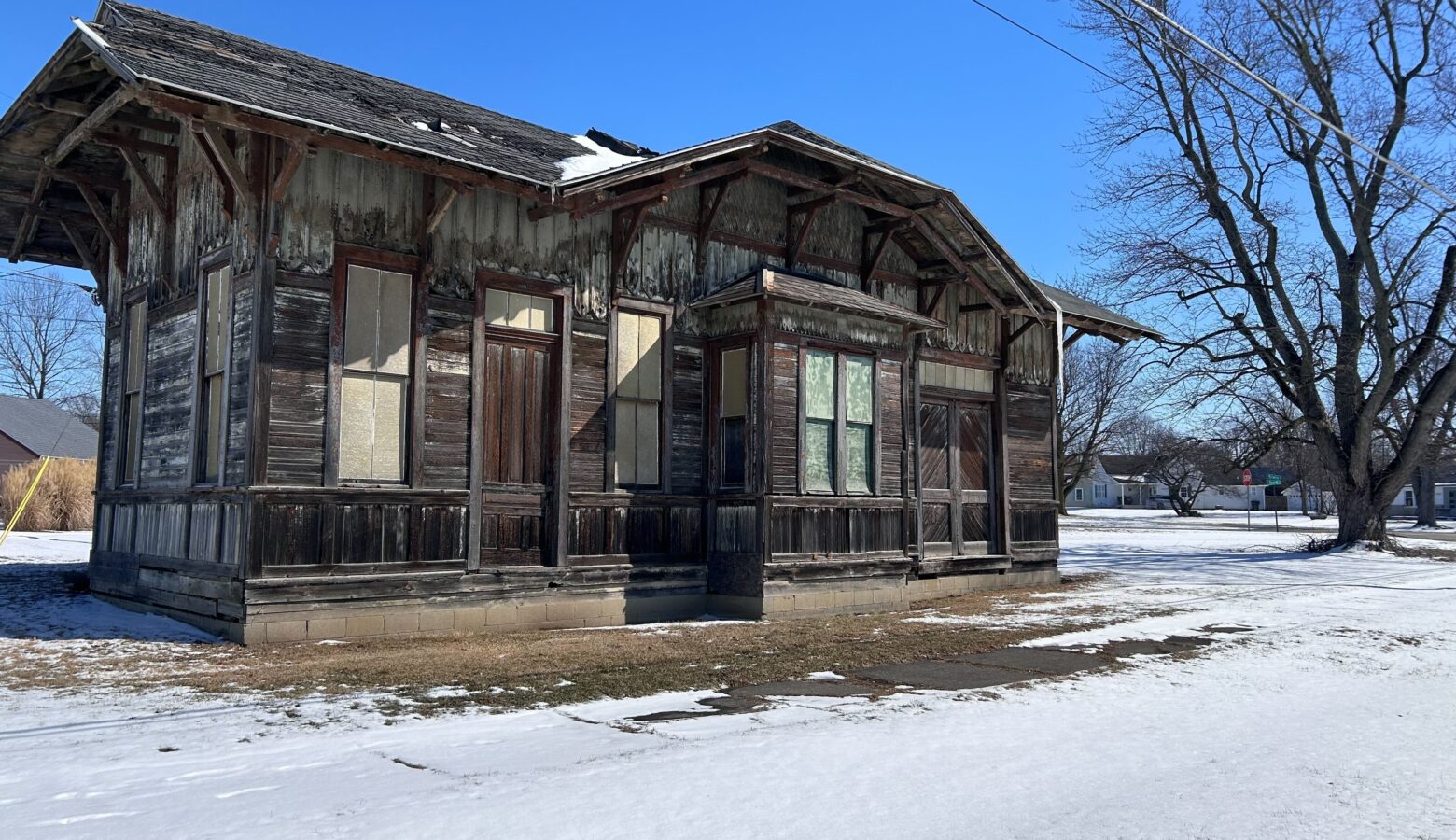 An old building with broken wooden paneling stands surrounded by snow.