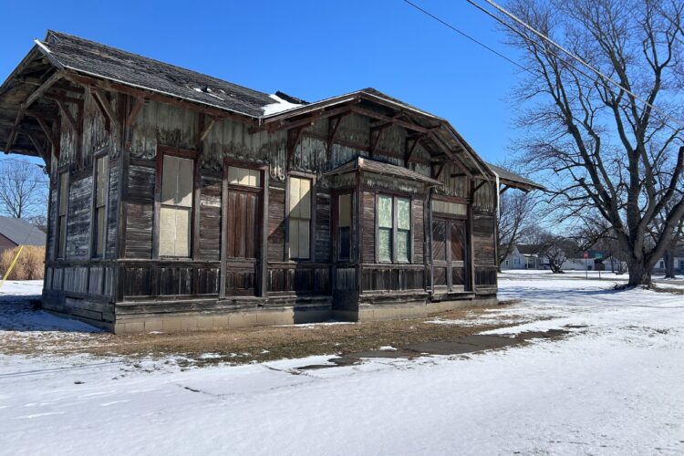 An old building with broken wooden paneling stands surrounded by snow.