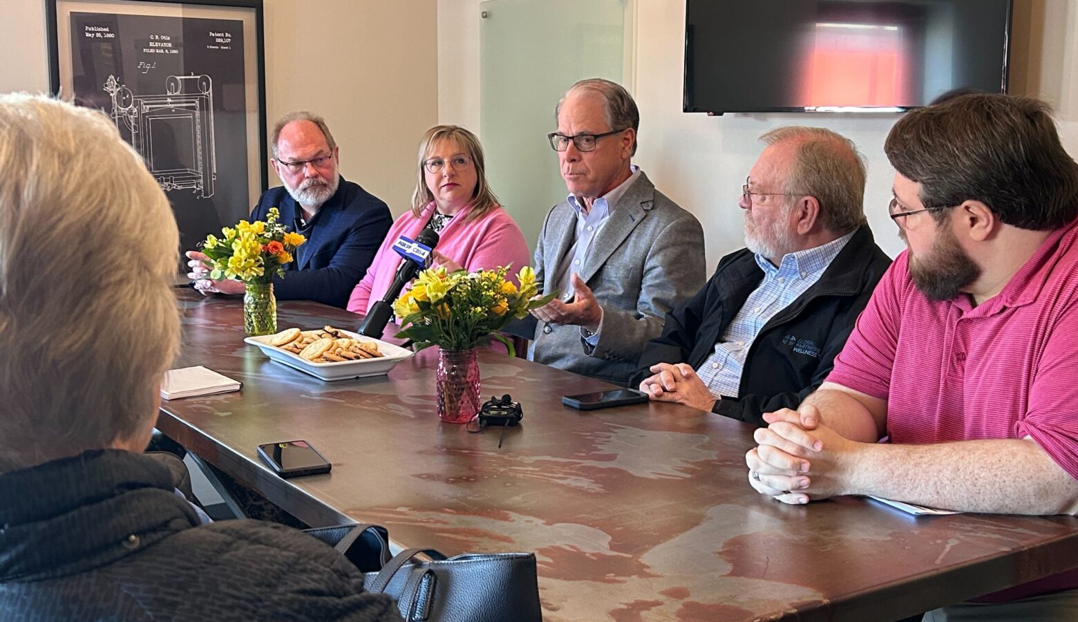 Gov. Mike Braun, an older White man in a suit, sits around a table with people listening to him speak.