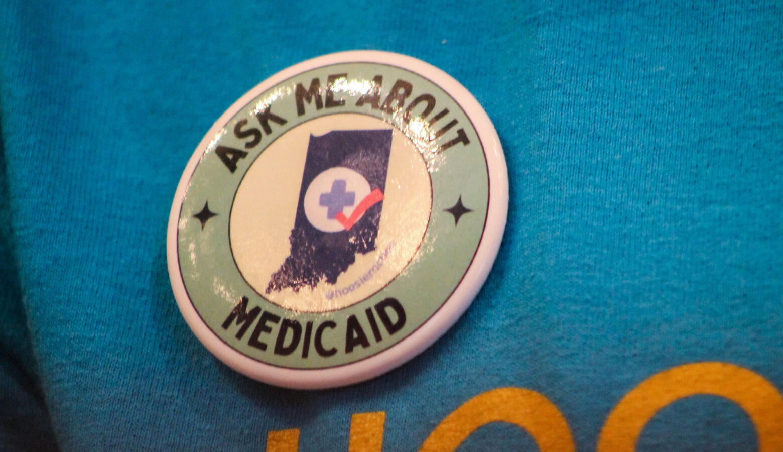 A button is pinned to a bright blue shirt that says "Ask me about Medicaid."