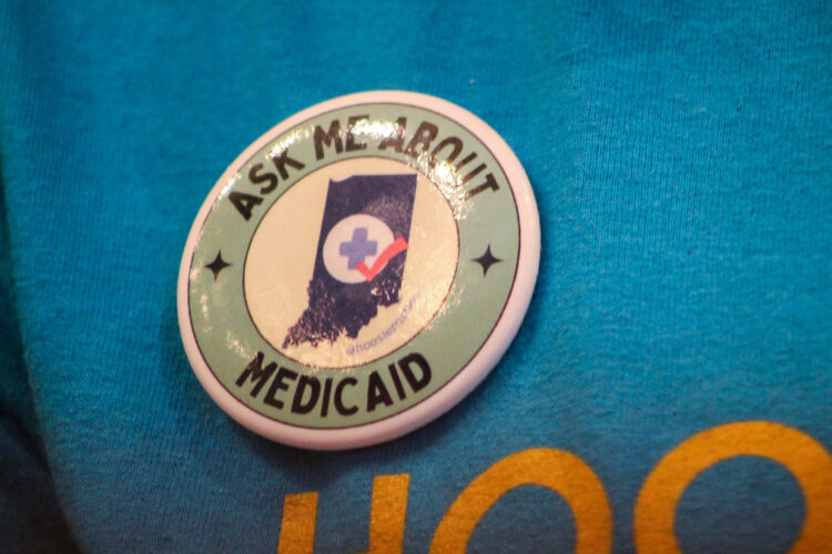 A button is pinned to a bright blue shirt that says "Ask me about Medicaid."