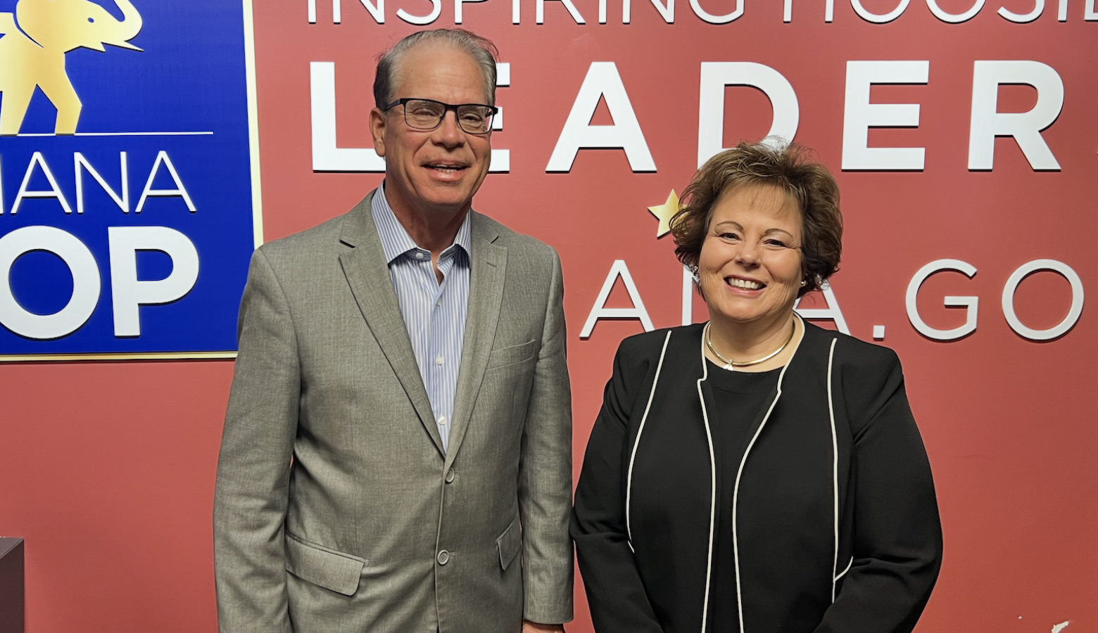 Mike Braun stands next to Lana Keesling. Braun is a White man, balding with dark hair. He is wearing glasses and a tan suit jacket. Keesling is a White woman with dark hair. She is wearing a black suit.