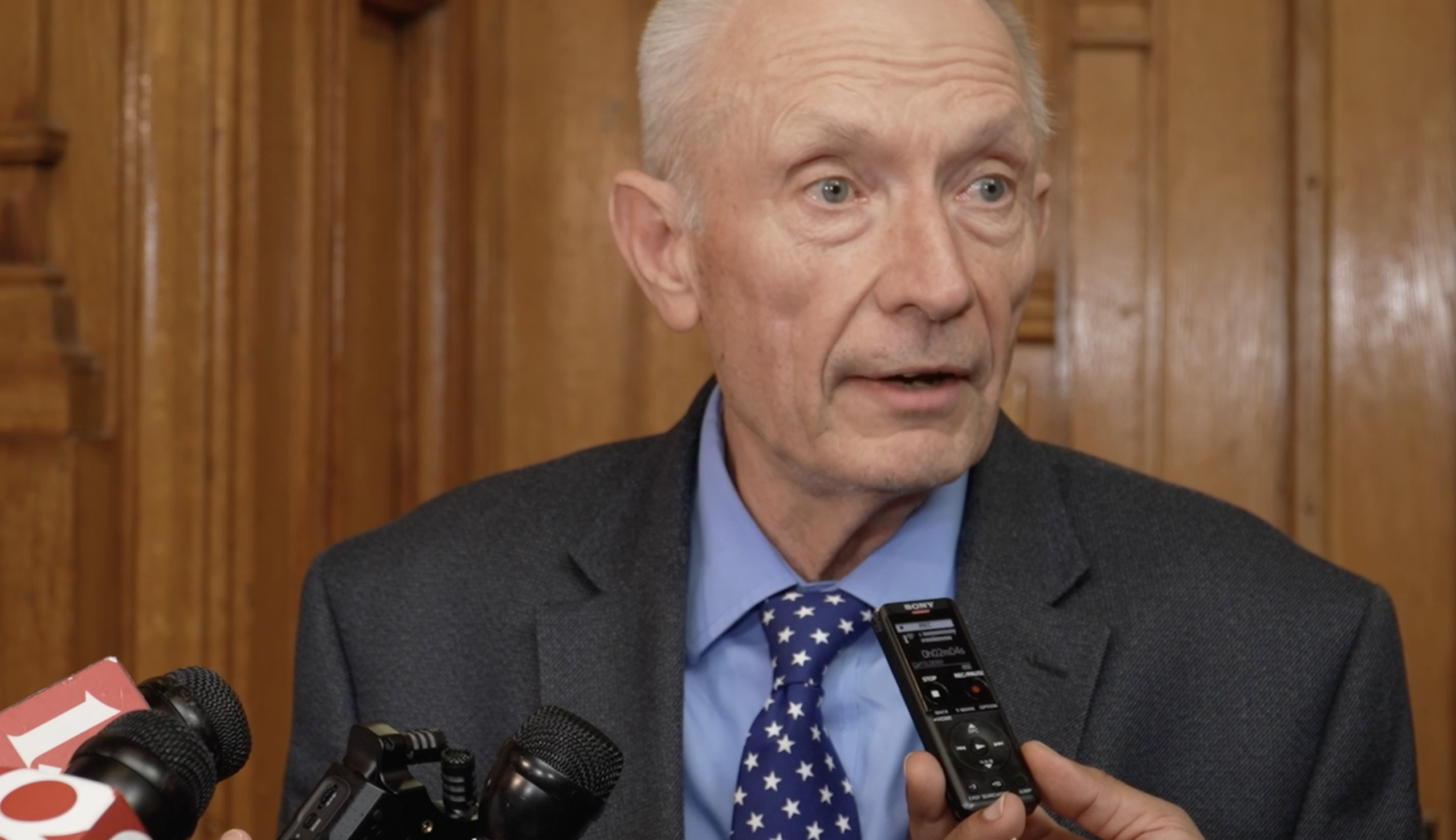 Jeff Thompson speaks with reporters. Thompson is a White man with white hair. He is wearing a gray suit.