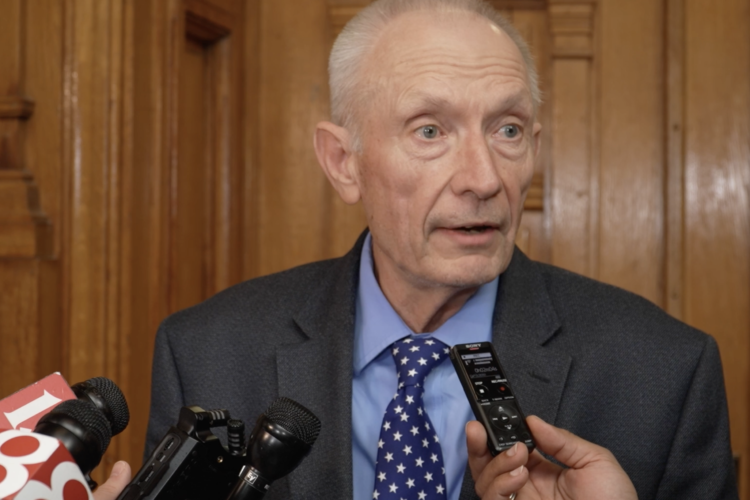 Jeff Thompson speaks with reporters. Thompson is a White man with white hair. He is wearing a gray suit.