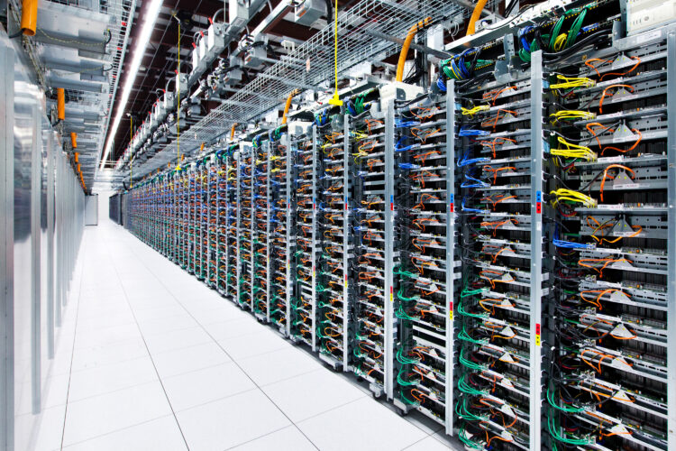 Server racks stretch down a long hallway. The tiled floor is white and wires poke neatly out of the metal racks.