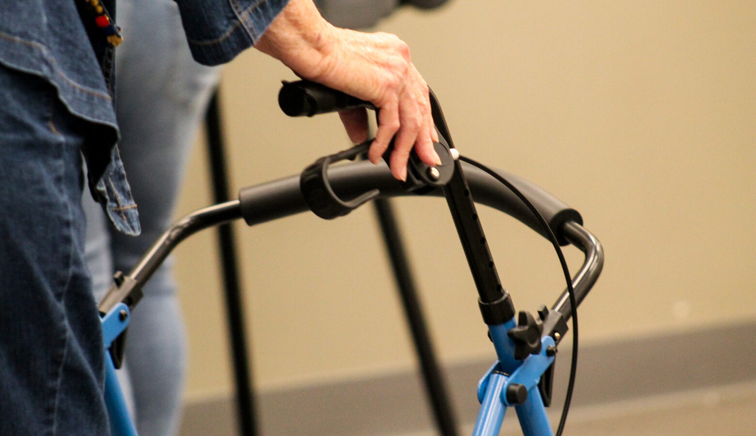 A older person in a jean jacket and jeans uses a walker as a mobility aid.