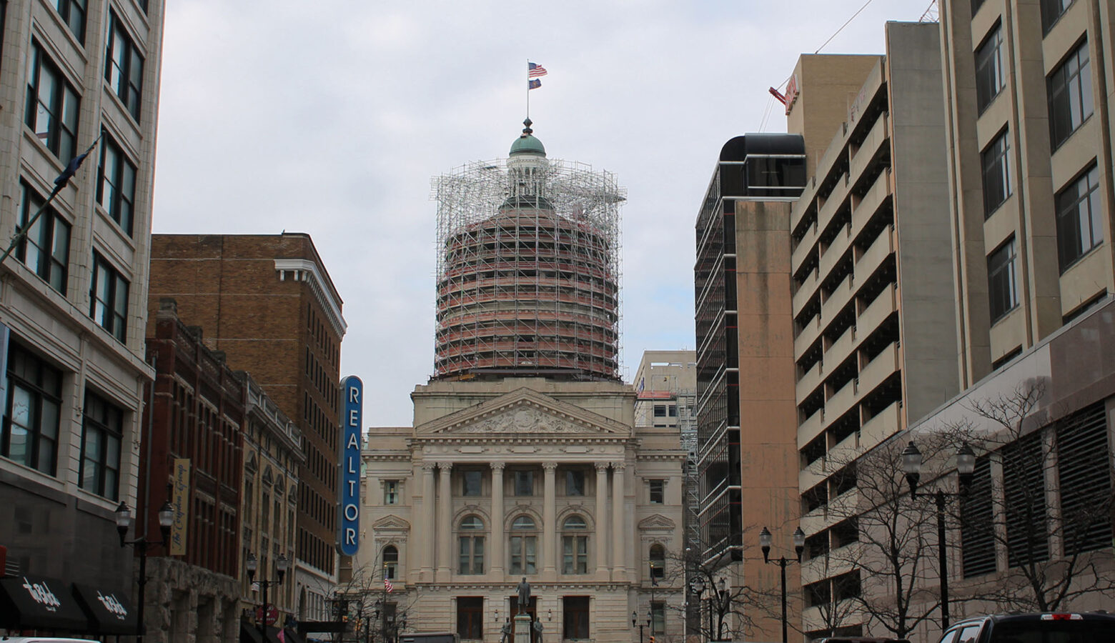 The eastern exterior of the Indiana Statehouse, framed between other buildings in downtown Indianapolis.