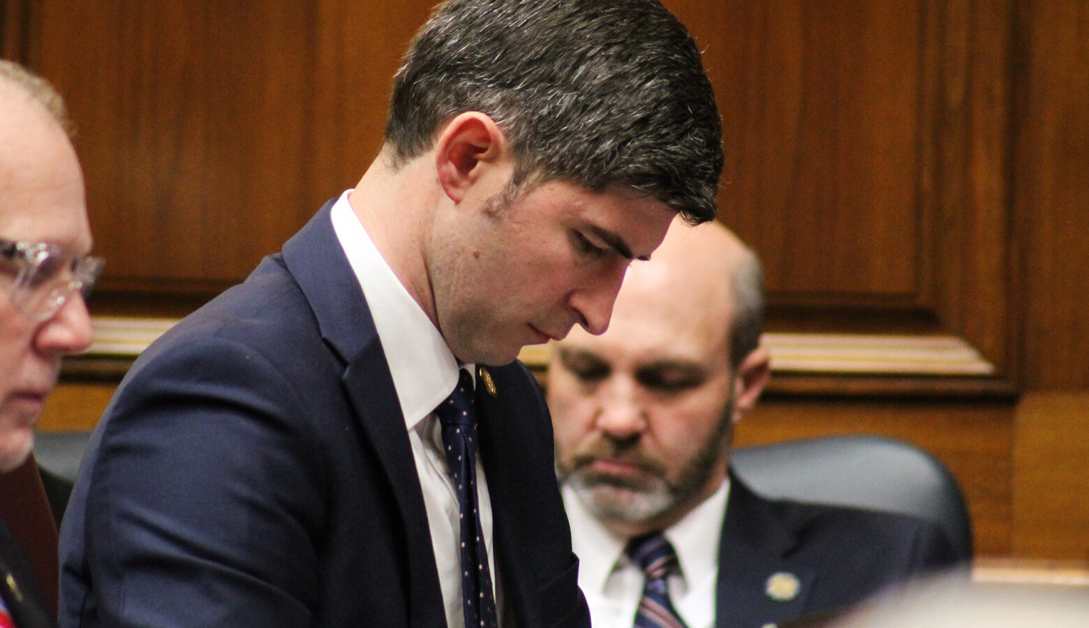 Tim Wesco listens to a speaker from his desk on the House floor. Wesco is a White man with dark hair. He is wearing a suit and tie.