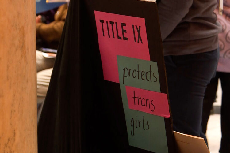 A poster board at a protest reads "Title 9 protects trans girls."