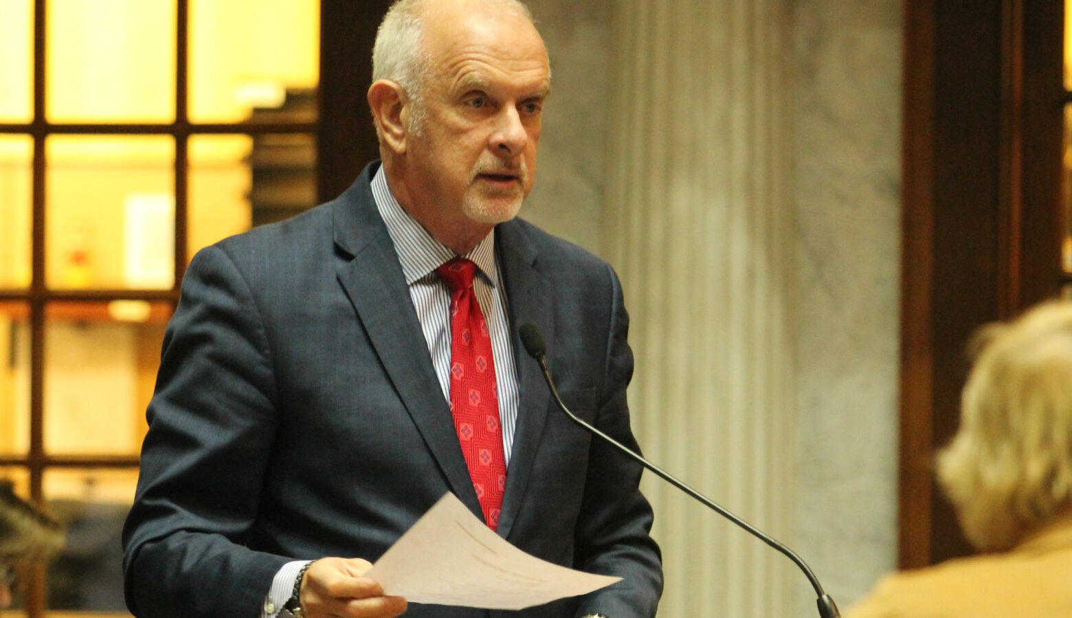 Travis Holdman speaks on the Senate floor. He is a White man, balding with white hair. He is wearing a suit and tie.