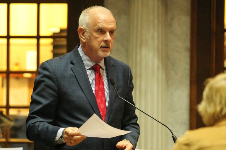 Travis Holdman speaks on the Senate floor. He is a White man, balding with white hair. He is wearing a suit and tie.