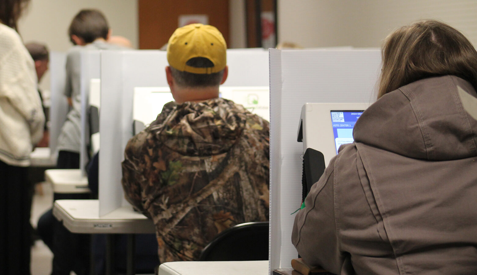 A group people sit at voting booths with digital screens.