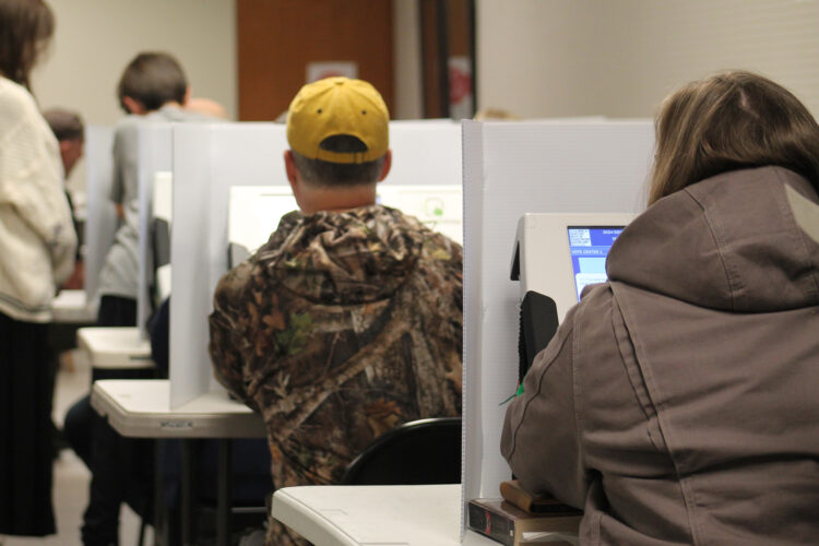 A group people sit at voting booths with digital screens.