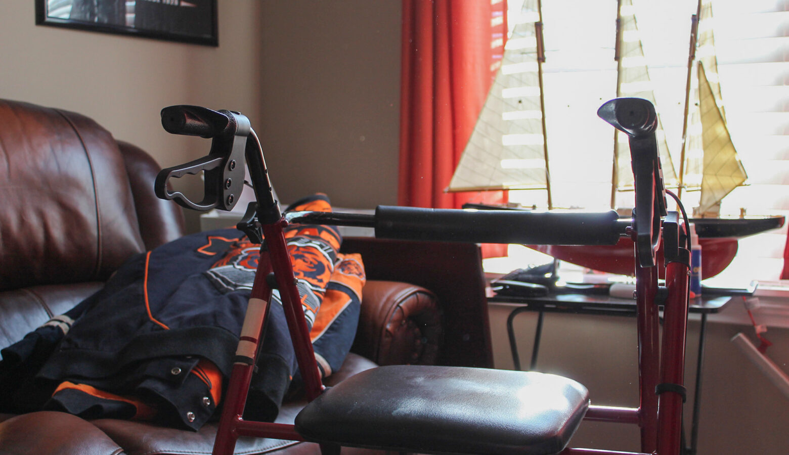 A walker sits in front of a leather couch with a Chicago Bears jacket on it.