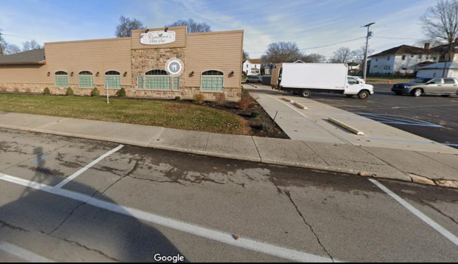 A tan brick building is seen from its side, next to a parking lot with two trucks.