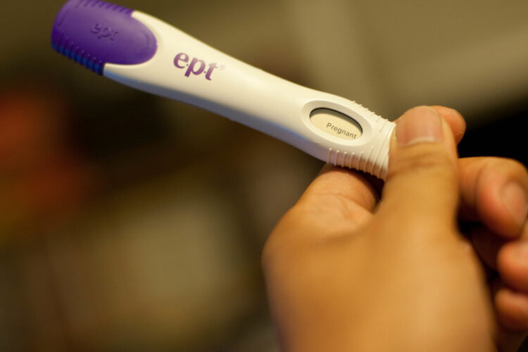 An unseen person holds a digital pregnancy test. It says "Pregnant"