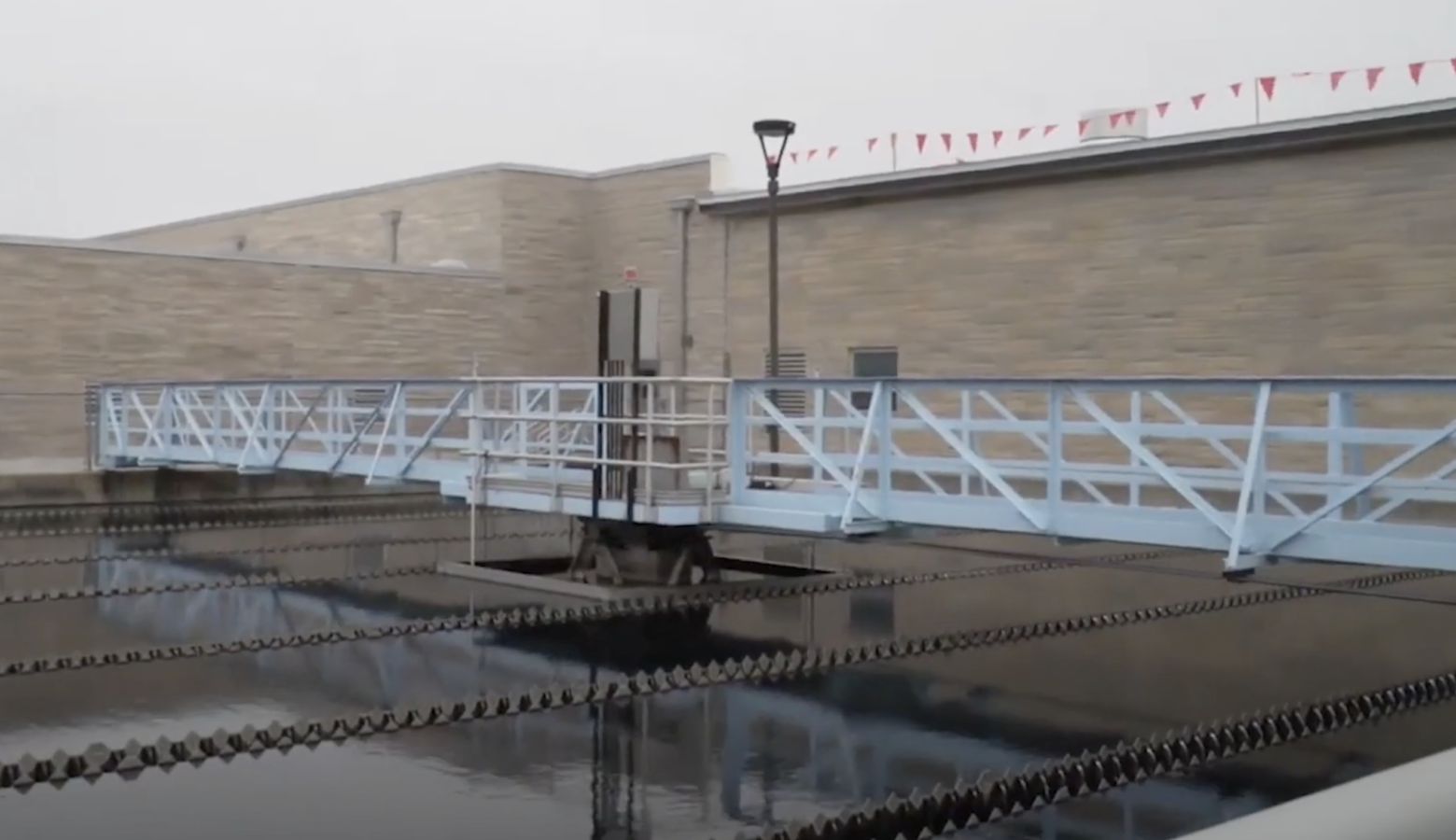 A pool of water reflects a white metal bridge and a brick wall at the City of Bloomington Utilities' water treatment plant.