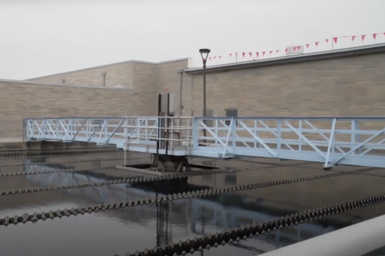 A pool of water reflects a white metal bridge and a brick wall at the City of Bloomington Utilities' water treatment plant.