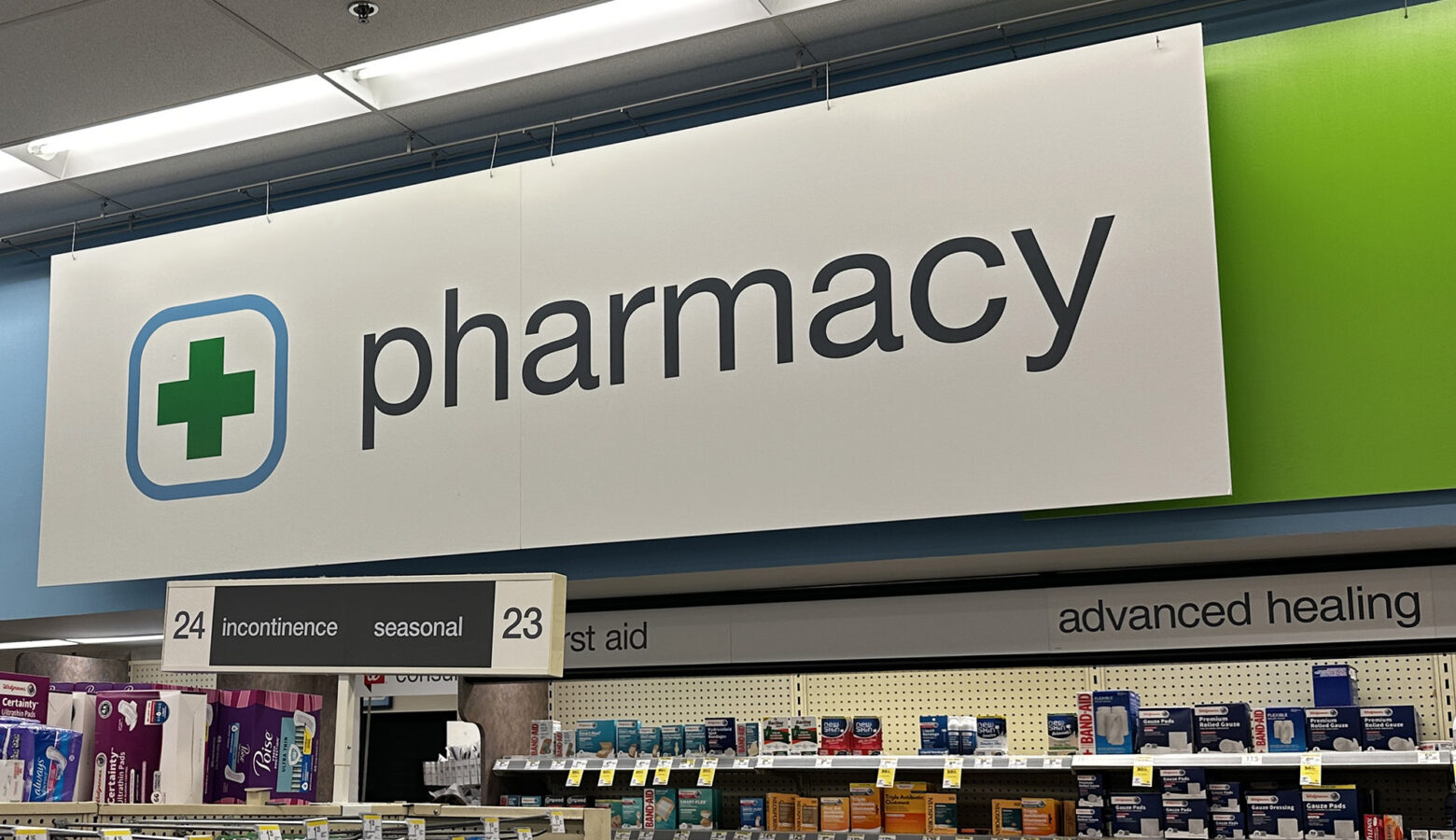 A sign hangs inside a store that says "pharmacy" in all lowercase letters in front of a light blue and lime green wall.