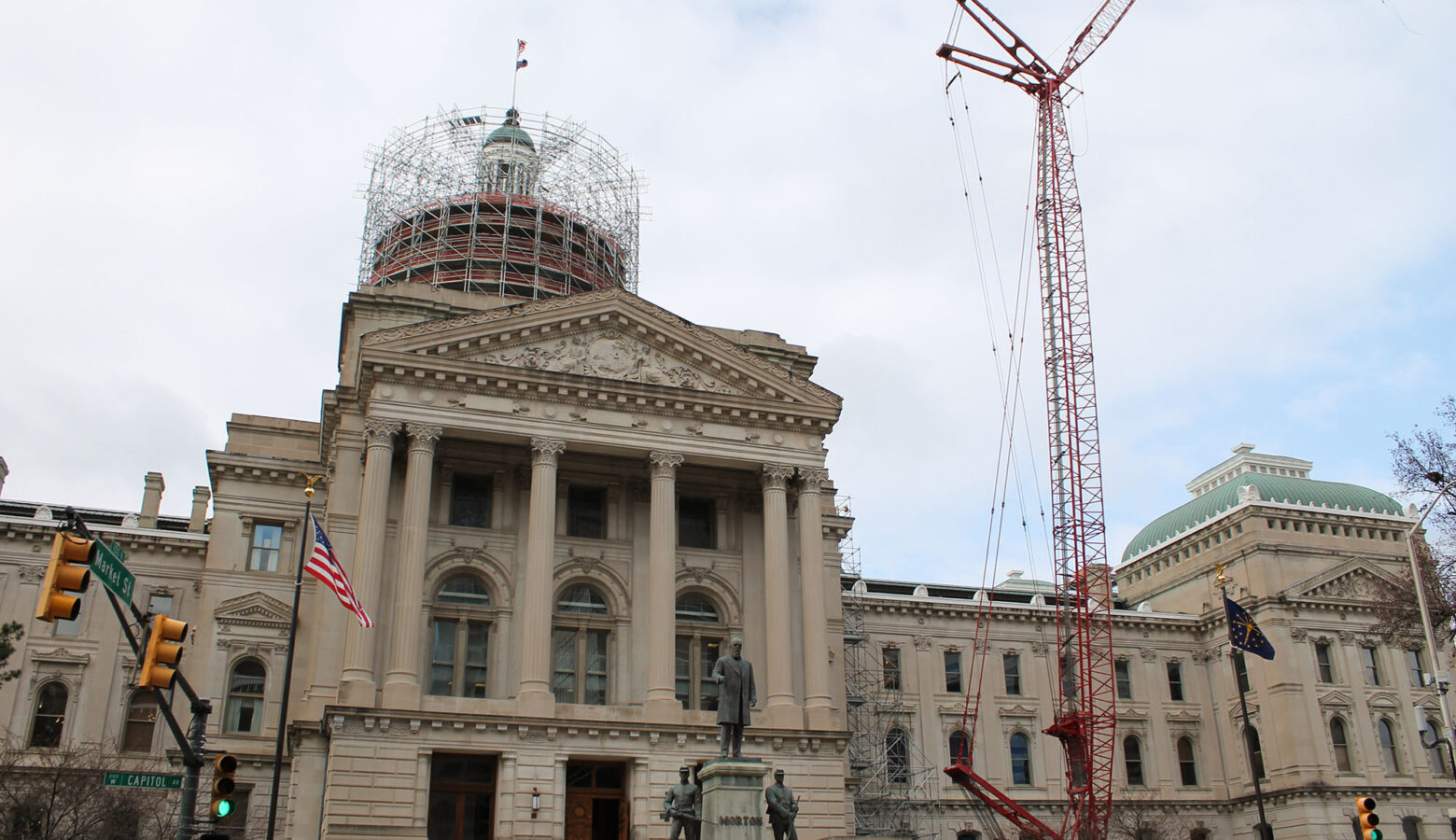 The Indiana Statehouse sits against a blue sky with a red construction crane visible to the right and scaffolding around the cupola.