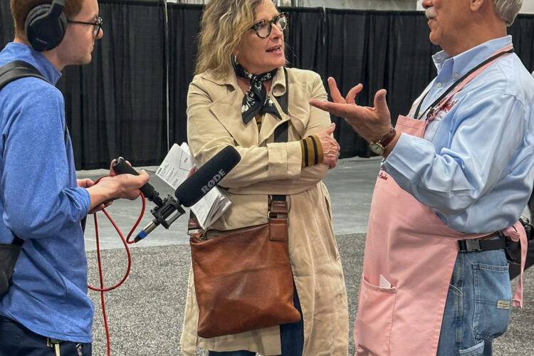 A man holds up a microphone to a woman and a man talking and laughing.