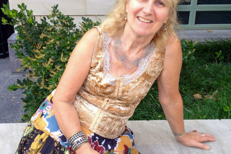 A woman sits on a concrete bench and smiles up at the camera.