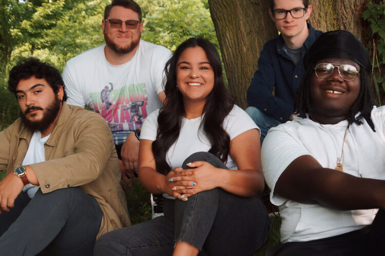Five people sit under a tree smiling.