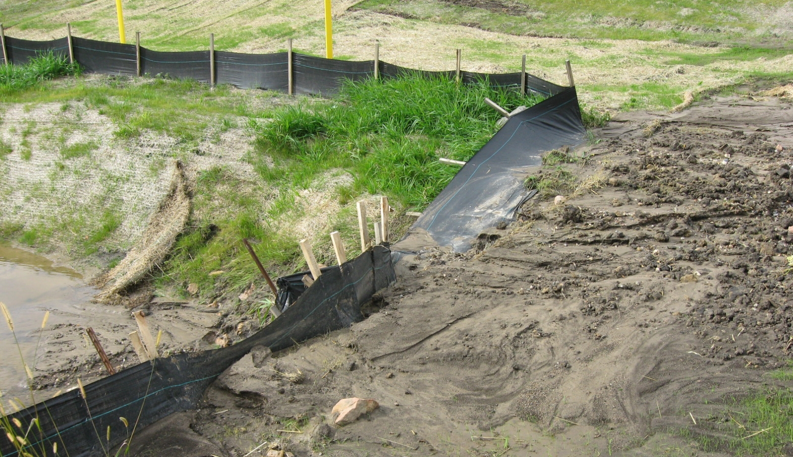 A grassy incline with dirt looks to be spilling over a black tarp fence.