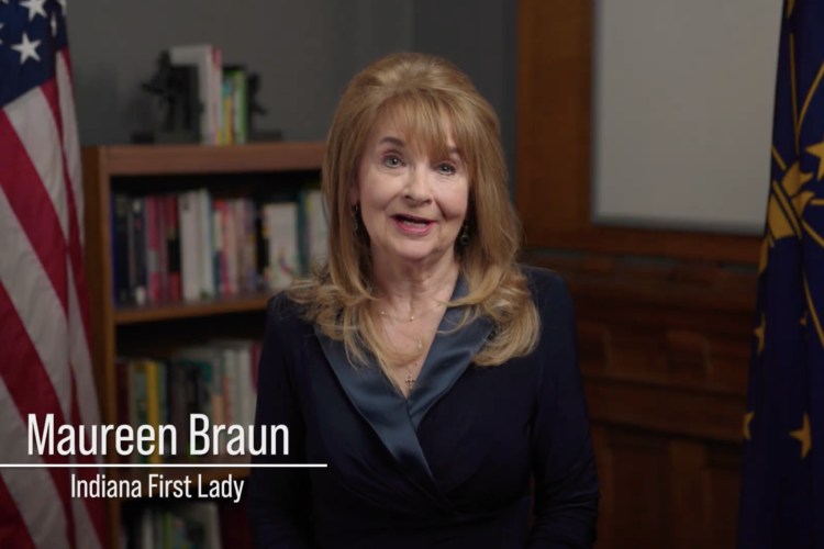 A still image of a video of Maureen Braun. Braun is looking directly into camera and her name and title are in the lower left corner. Braun is a White woman with light brown hair. She is wearing a black jacket over a dark blue top.