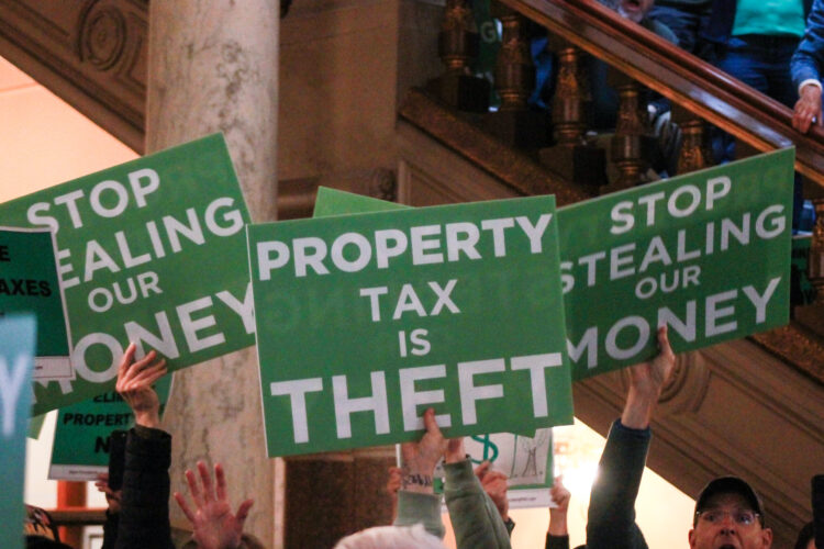 People hold up signs that read "Property Tax is Theft" and "Stop Stealing Our Money"
