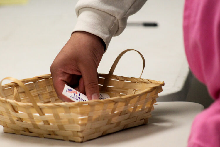 A hand reaches into a basket of stickers with small printed American flags that say "I Voted Early."