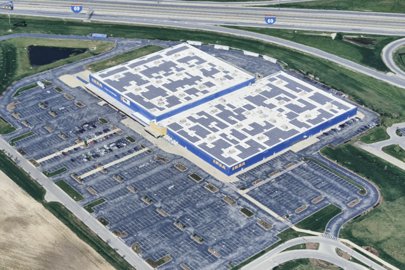 A Google Earth screenshot shows an aerial view of the Ikea in Fishers. The roof of the massive building is littered with neat, geometric clusters of solar panels. The building is painted blue with "IKEA" written in yellow font at its corners. In the top portion of the image is a highway, labeled by Google Earth as Interstate 69. 