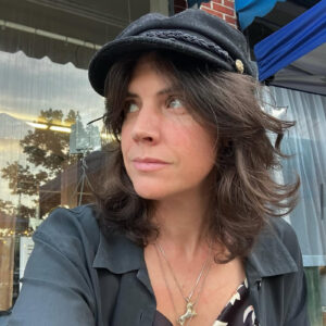 A woman in a black fabric cap and jacket looks up and away from the camera.