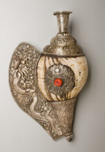 Ornate Tibetan conch shell horn wrapped in silver, featuring detailed floral and dragon motifs, a coral inlay, and a flared mouthpiece.