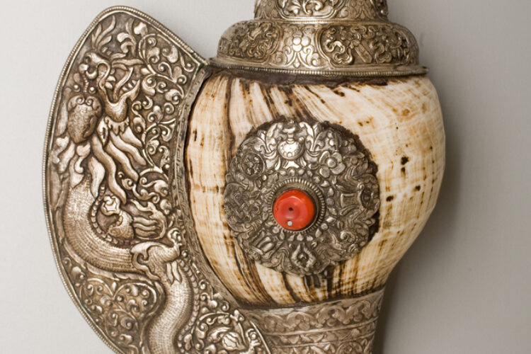 Ornate Tibetan conch shell horn wrapped in silver, featuring detailed floral and dragon motifs, a coral inlay, and a flared mouthpiece.
