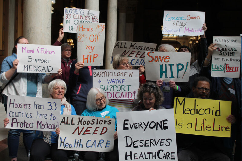 People gathered at a rally inside the Statehouse holding signs that say “Hoosiers from 33 counties here to Protect Medicaid,” “Hands off my HIP,” “All Hoosiers need Healthcare,” “Everyone deserves healthcare,” “Medicaid is a lifeline,” “Save HIP,” “We deserve a health care system that puts people’s lives before profits” and several more referencing specific counties.