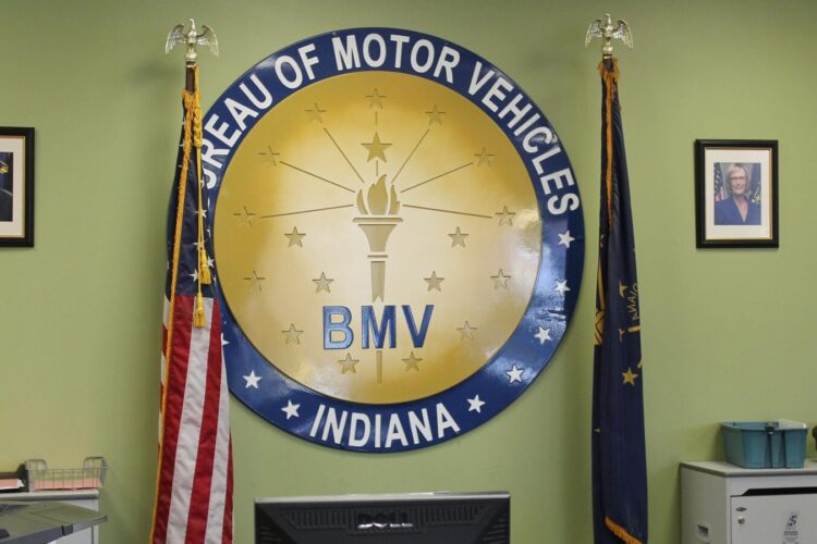 The Indiana BMV seal hangs on a green wall, surrounded by the American and Indiana flags.
