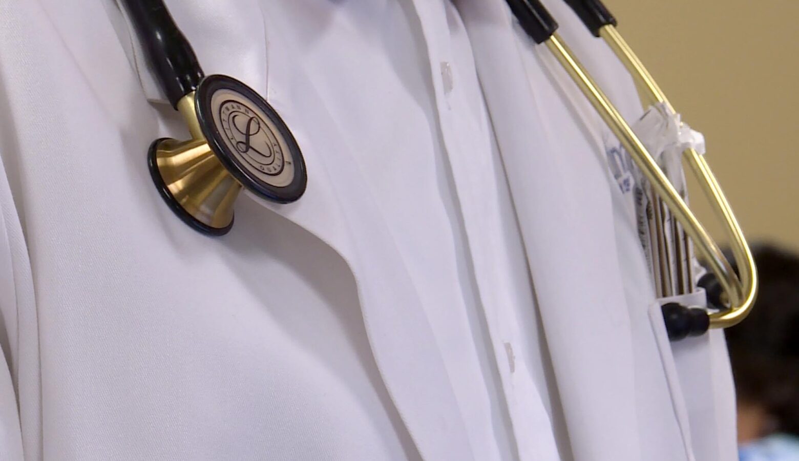 A doctor's white lab coat over a white button down shirt. A stethoscope hangs around the doctor's neck.