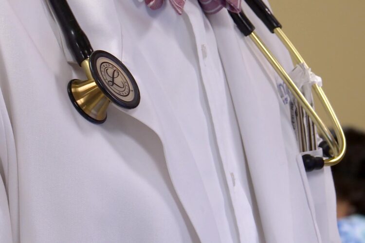 A doctor's white lab coat over a white button down shirt. A stethoscope hangs around the doctor's neck.