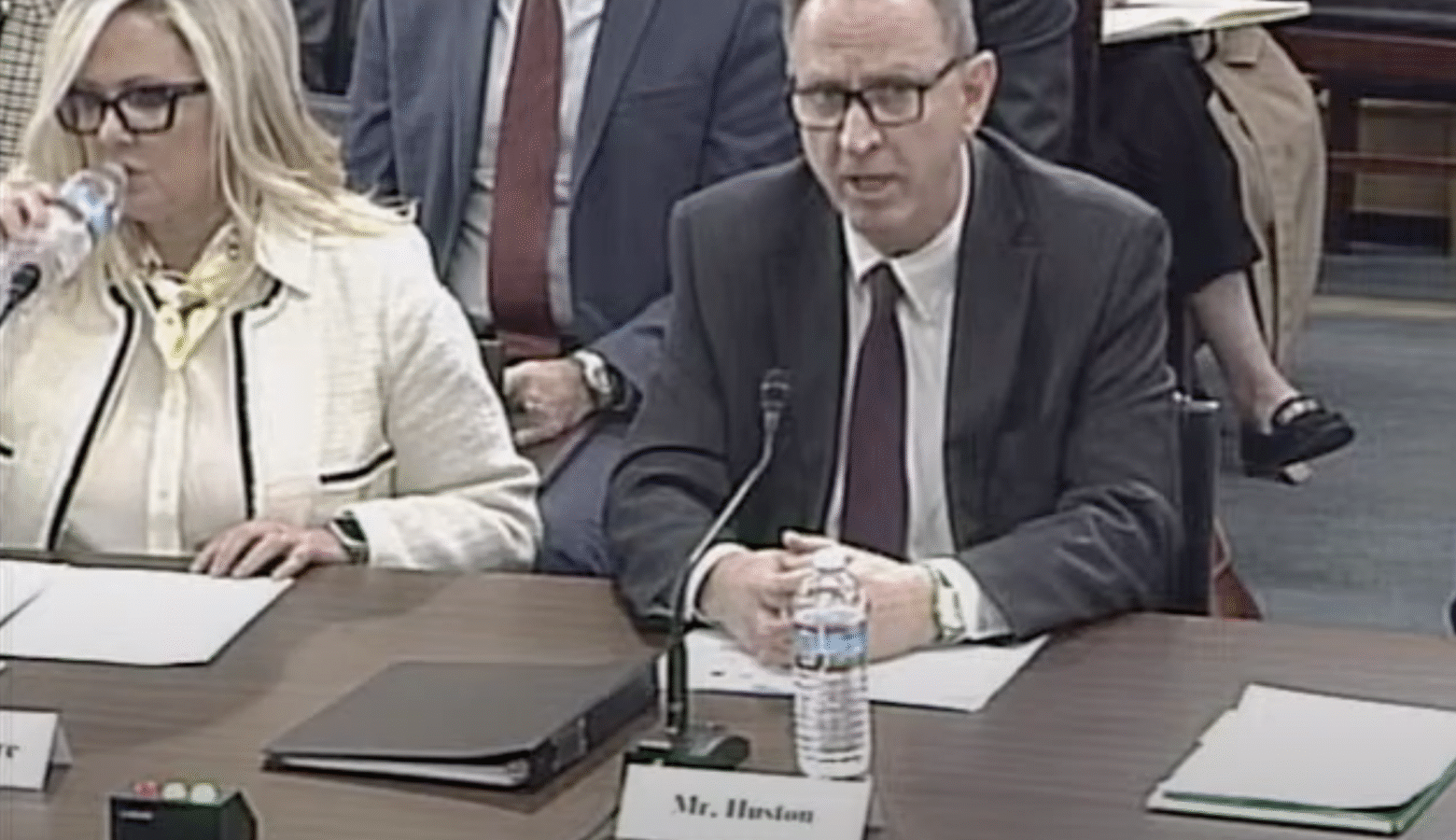 IURC Chairman Jim Huston speaks at a U.S. House Committee on Energy and Commerce hearing on the challenges state utility regulators face in delivering reliable and affordable energy. He is a White man, wearing glasses and a suit. He sits at a table with papers, microphone, water bottle and a small paper name plate that says Mr. Huston.