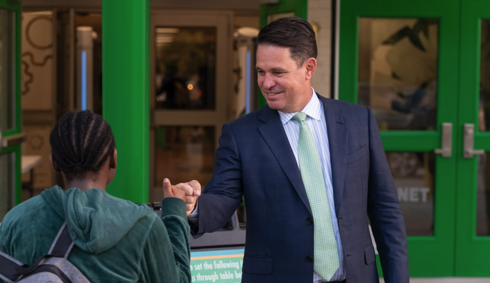 New Ivy Tech President Marty Pollio, dressed in a suit with a green tie, fist bumps with a student.