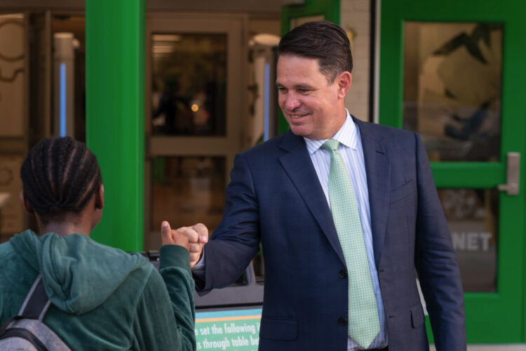 New Ivy Tech President Marty Pollio, dressed in a suit with a green tie, fist bumps with a student.