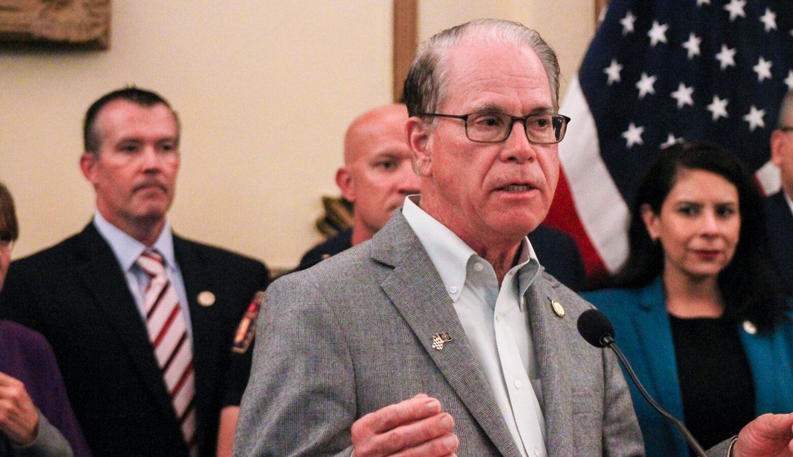 Mike Braun is a White man, balding with dark gray hair. He is wearing glasses and a gray sport coat over a white shirt. Aaron Freeman is a White man with dark hair. He is wearing a black suit with a blue shirt and a white and red striped tie.